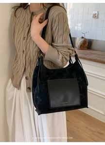 Close-up of black suede tote bag featuring a leather square pocket and gold brand logo