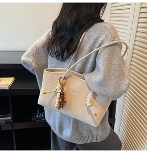 Detail of off-white PU leather tote bag with vintage beaded pendant and branded logo