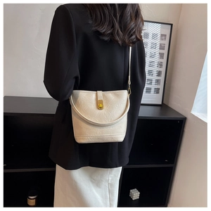 Chic off-white bucket bag with gold clasp shown on model with black suit and white skirt