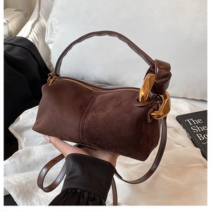 Detail of dark brown suede handbag featuring gold chain link and metallic zipper closure