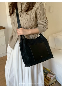 Detail of black suede tote bag with leather pocket paired with elegant beige knitwear