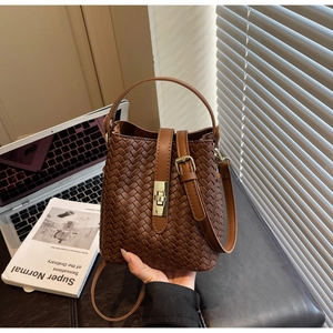 Detail of a brown woven bucket bag with a golden metal lock and an adjustable strap