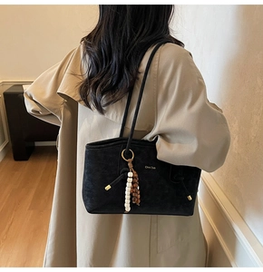 Detail of black suede tote bag with stylish beaded tassel and brand logo on model