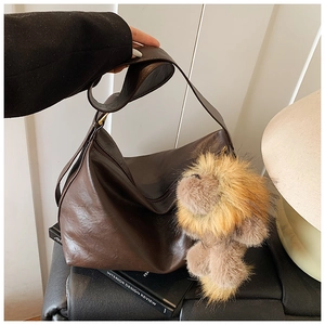Gros plan d'un sac hobo marron foncé en cuir brillant avec un porte-clés lion en peluche