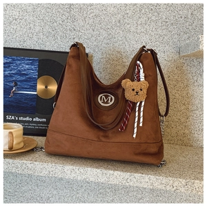 Gros plan détaillé d'un sac cabas en daim marron foncé avec logo M et breloque en peluche