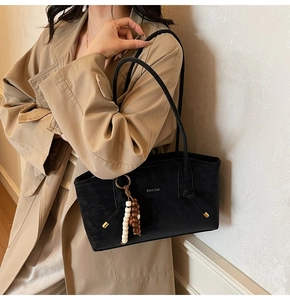 Detail of black matte tote bag with elegant beaded tassel and brand logo on shoulder