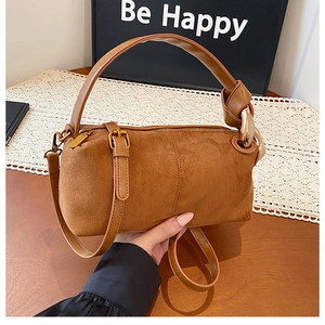 Detailed close-up of brown suede cylinder bag with gold hardware and leather strap