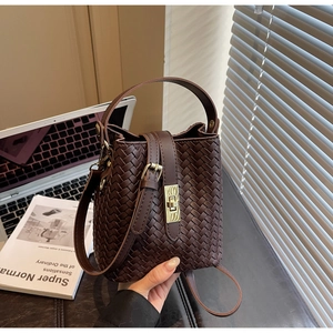 Detail of woven brown bucket bag with gold metal twist lock on a modern workspace desk