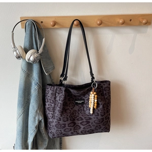 Detail of leopard print tote bag with leather straps and wooden bead charm on a wooden hook