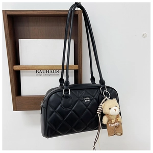 Close-up of black quilted shoulder bag with brand logo and cute plush bear accessory