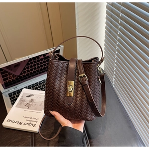 Detail of deep brown woven leather bucket bag with golden buckle on a lifestyle background