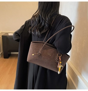 Detail of dark brown suede tote bag featuring gold lettering and beaded charm pendant