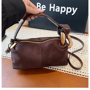 Detail of dark brown suede handbag featuring a bold gold metal ring handle and zipper