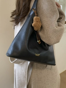 Chic black leather tote bag with star pendant on beige coat background, side view