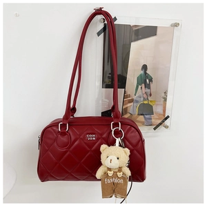 Detail of burgundy quilted leather handbag featuring a teddy bear charm and sleek straps