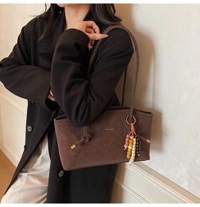 Detail of dark brown leather tote featuring beaded charm and knotted strap accent