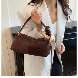 Close-up of brown suede pillow bag featuring gold metal chain link handle detail