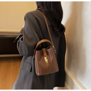 Detail of a brown woven bucket bag featuring gold rectangular clasp and slim shoulder strap