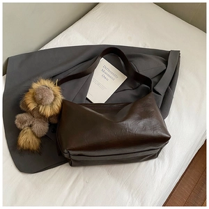 Détail du sac cabas en cuir marron foncé avec un pendentif peluche sur la bandoulière
