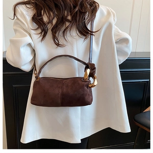 Detail of dark brown suede handbag featuring a bold gold metal ring buckle and fine strap