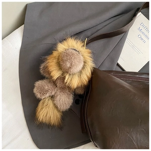 Détail d'un bijou de sac lion en peluche sur une poignée de sac en cuir marron