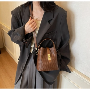 Detail of a brown woven leather bucket bag featuring a gold lock and top handle