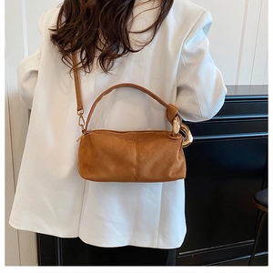 Detail of caramel brown matte handbag with gold metal hardware on model in white blazer