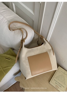 Detail view of a minimalist cream and tan suede shoulder bag on a cozy white sofa