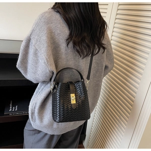 Detail showing the woven texture and golden clasp of the black bucket bag on a model