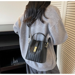 Detail of black woven bucket bag showing intricate leather texture and gold buckle clasp
