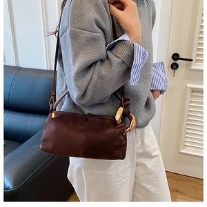 Deep brown suede shoulder bag with gold metal rings shown on model in home setting