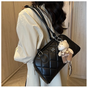 Detail of black quilted shoulder bag featuring silver metal logo and plush bear charm accessory