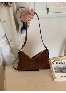 Détails de la texture en daim mat et de la fine bandoulière en cuir de ce sac marron