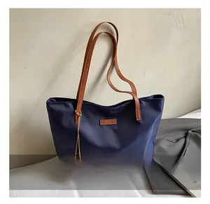Dettaglio della grande borsa tote in nylon blu navy con manici in pelle e ciondolo rotondo