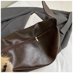 Détail d'un grand sac bandoulière en cuir marron foncé avec fermeture éclair et charm
