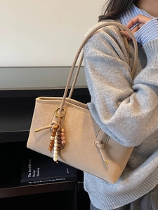 Beige tote bag with wooden bead tassel shown from a side view in a cozy room setting