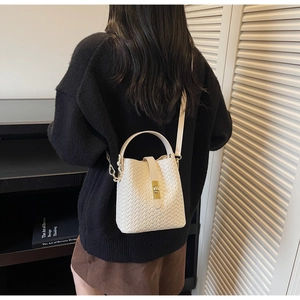 Detail of white woven leather bucket bag with cross-weave texture and gold twist lock