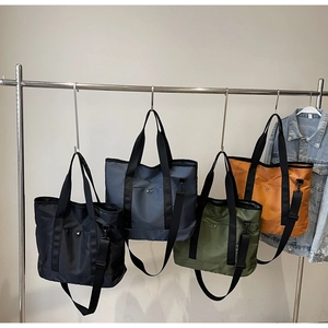 Close-up of four canvas tote bags in black, blue, green, and orange on a metal rack
