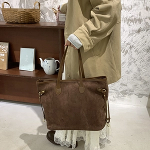 Detail of brown suede tote bag featuring side drawstrings and slender shoulder straps