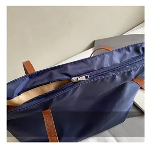 Dettaglio della borsa tote in nylon blu navy con manici in pelle marrone e zip argento