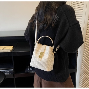 Detailed view of white woven bucket bag with gold clasp and adjustable shoulder strap