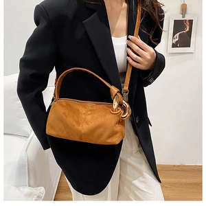 Detail of caramel brown suede handbag showing large gold metal rings and zipper closure