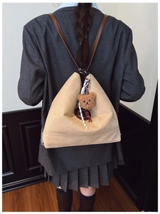 Détail du sac à dos en daim marron clair avec logo en métal et breloque ours en peluche