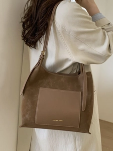 Large brown faux suede tote bag with leather pocket shown on a model in a minimal room