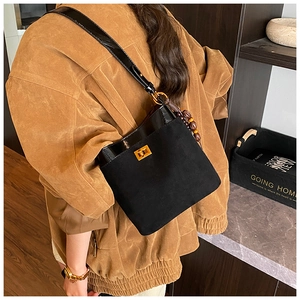 Detail of black suede shoulder bag featuring a gold twist lock and retro wooden bead charm