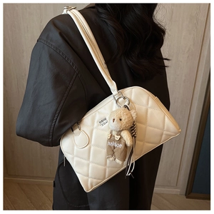 Close-up of a white quilted crossbody bag featuring a cute brown bear charm and metal logo