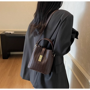 Detail of a dark brown woven bucket bag featuring a gold clasp and adjustable strap