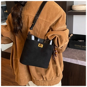 Detail of suede bucket bag with gold clasp and wooden bead charm on model shoulder