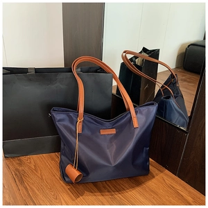 Dettaglio della borsa tote in nylon blu navy con manici in pelle marrone e logo