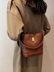 Brown vintage faux leather bucket bag with gold clasp shown worn as a crossbody bag